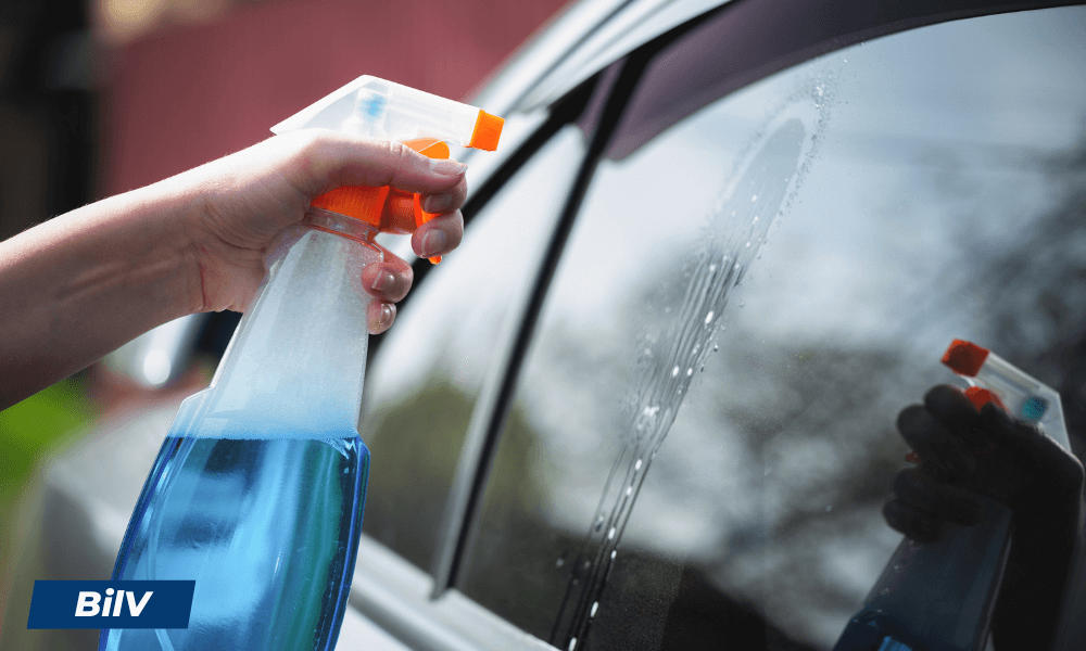 Hand som sprayar blå glasrengöring på bilruta med transparent rengöringsspray