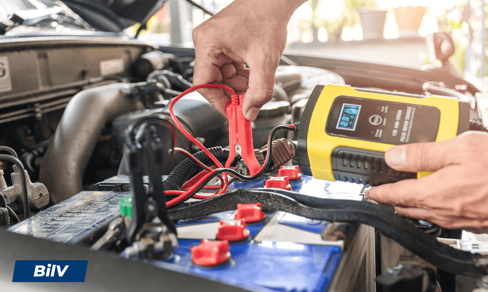 Man laddar bilbatteri med intelligent batteriladdare och krokodilklämmor för säker bilstart.